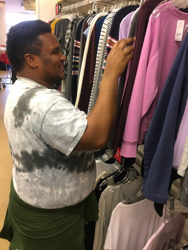 Man smiling looking through rack of clothes.