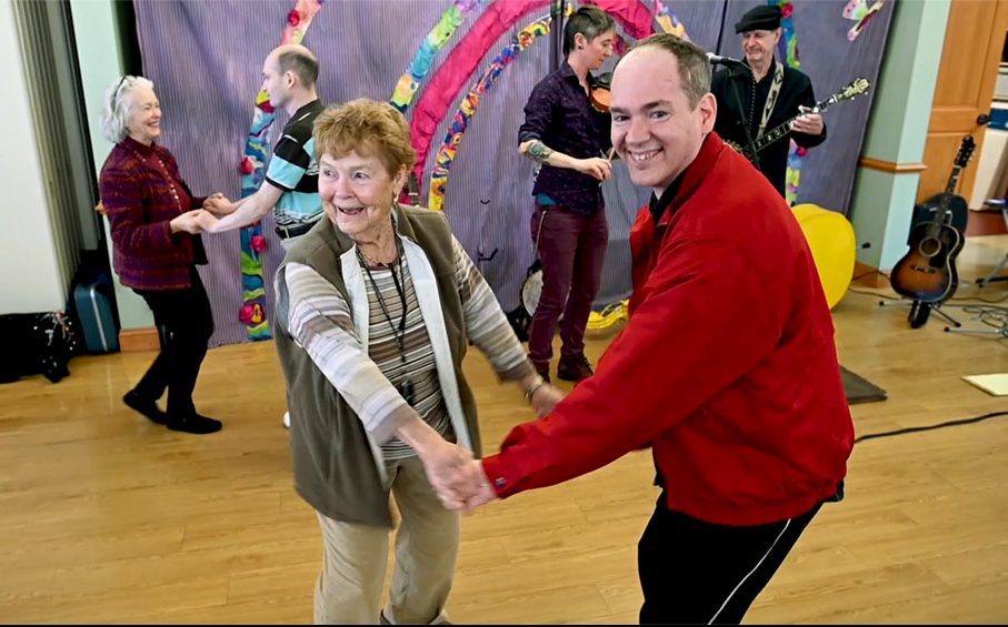 Young man dancing with older woman in front of acoustic musicians.